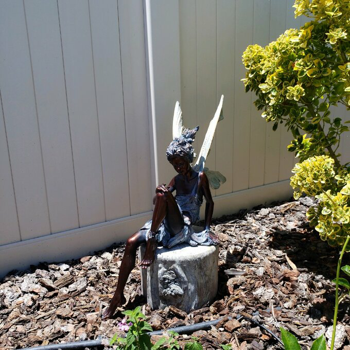 FairyGlo - Une statue de fée assise dans un jardin.