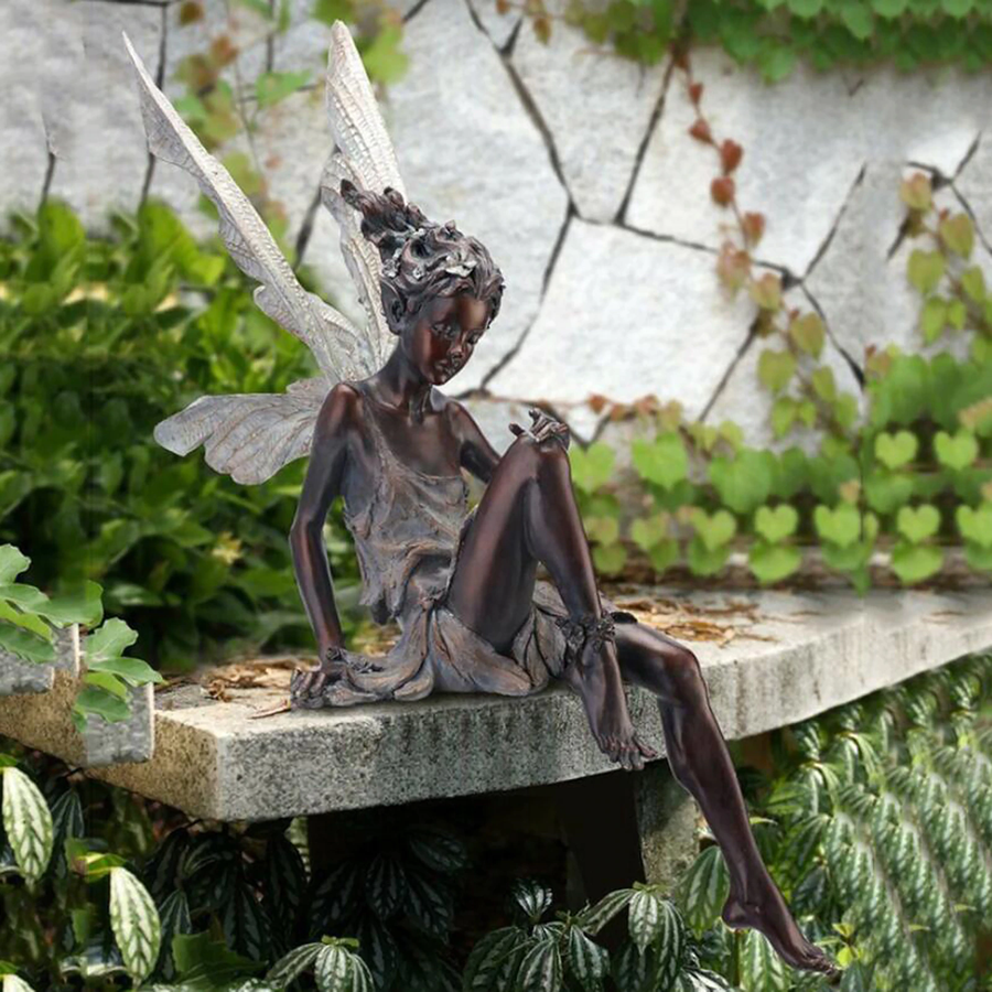 FairyGlo - Une statue de fée assise dans un jardin.