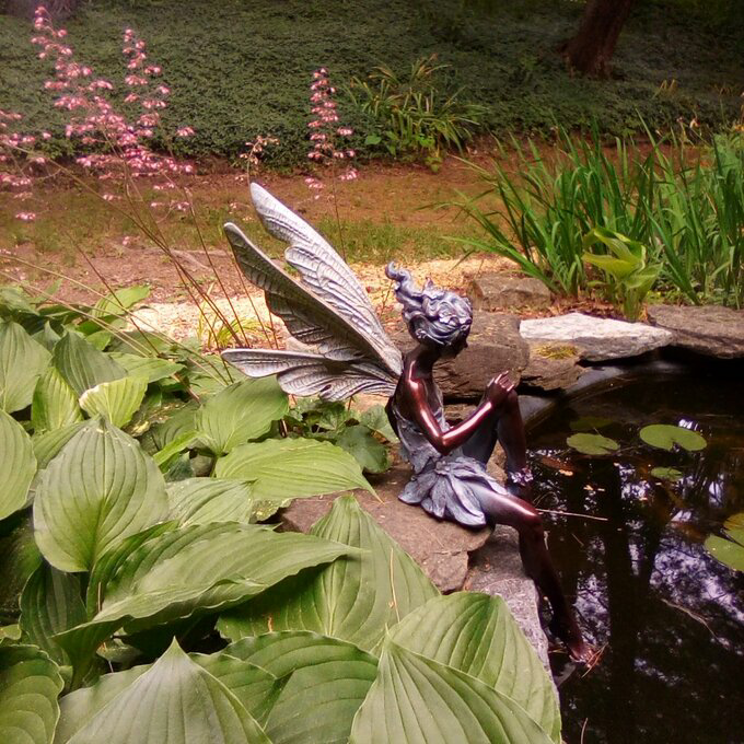 FairyGlo - Une statue de fée assise dans un jardin.