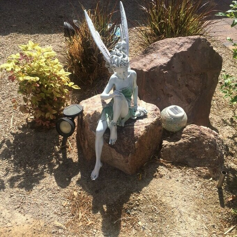 FairyGlo - Une statue de fée assise dans un jardin.