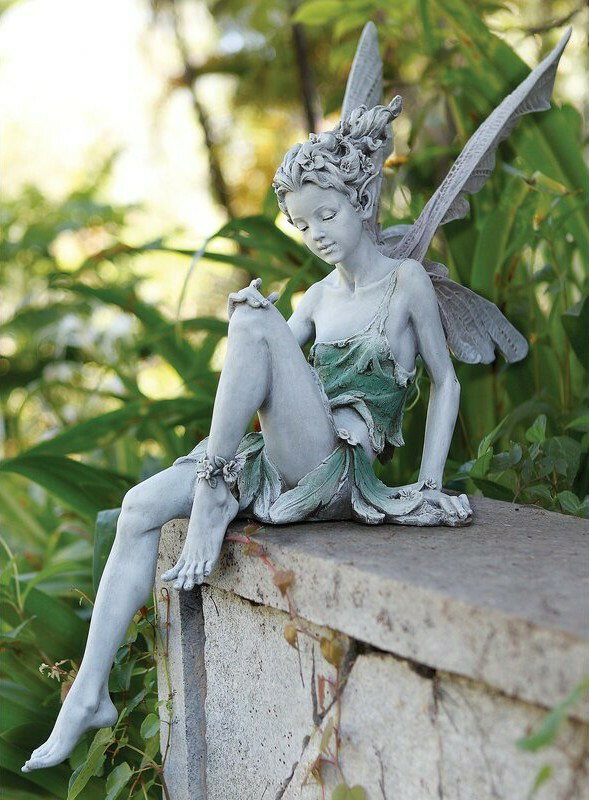 FairyGlo - Une statue de fée assise dans un jardin.